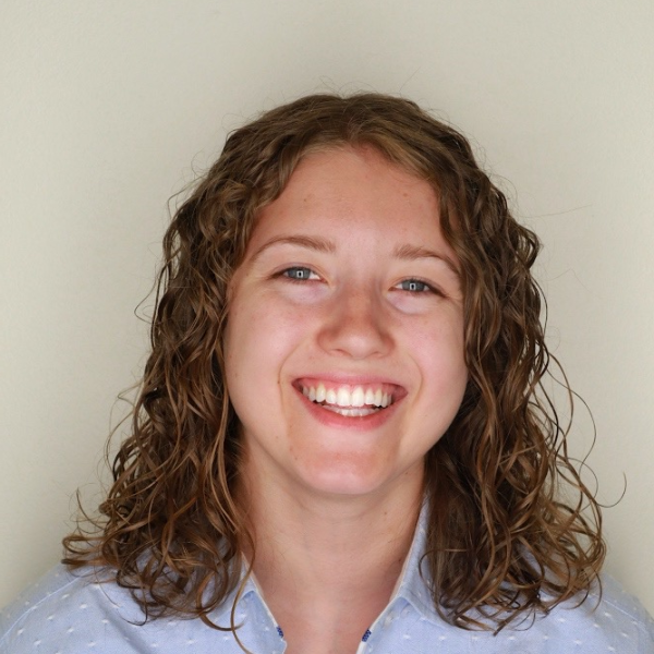 Portrait of Katie smiling with curly hair and a button down shirt.