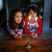 Two Asian American children look at a lit menorah